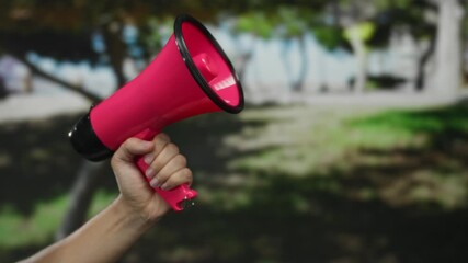 Hand holding pink megaphone in outdoor park setting with blurred greenery providing a vibrant background. - Powered by Adobe