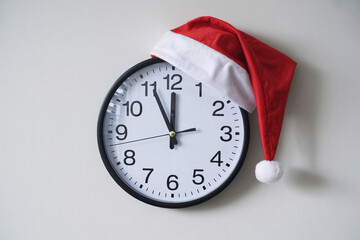 A Santa hat is on the office clock. The clock reads five to twelve.
