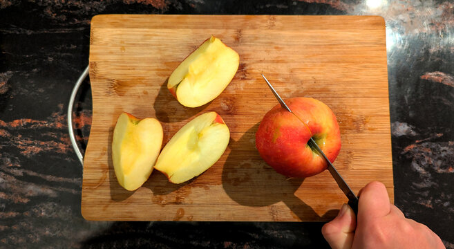 Hand cutting fresh red apple on wooden kitchen board