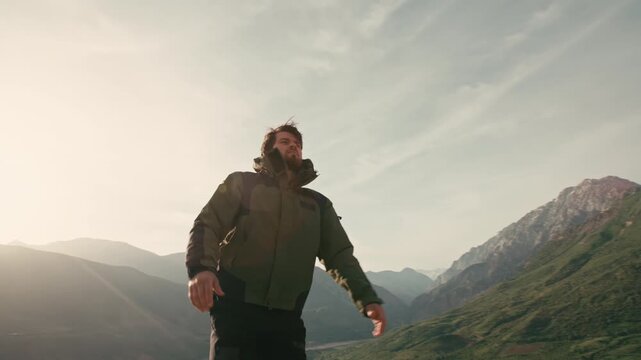 Traveler man standing on mountain trail raising arms to sky in morning sunlight camera moving around creating glowing lens flares concept of victory freedom joy and connection with nature