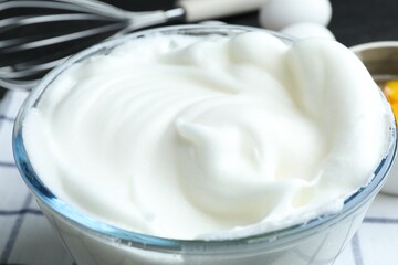 Whipped egg whites in bowl and whisk on table, closeup