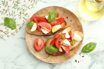 Tasty bruschettas with mozzarella cheese, tomatoes and basil on white marble table, flat lay