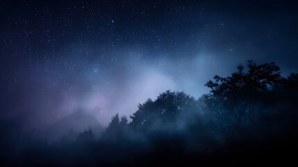 Naklejka premium A serene night sky filled with twinkling stars and a faint nebula seen above a misty silhouetted forest and distant mountains