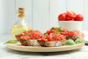 Tasty bruschettas with tomatoes and basil on white marble table, closeup