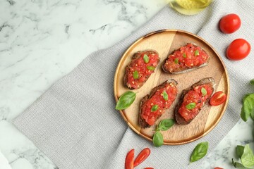 Tasty bruschettas with tomatoes and basil on white marble table, flat lay. Space for text