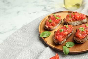 Tasty bruschettas with tomatoes and basil on white marble table, closeup. Space for text
