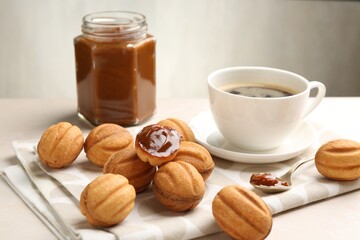 Delicious nut shaped cookies with boiled condensed milk and coffee on light table, closeup
