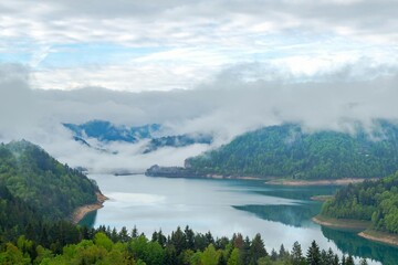 Lake surrounded by mountains and forest with clear sky and clouds