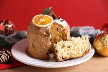Christmas food. Delicious Panettone cake and festive decor on beige table against red background, closeup