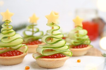 Christmas tree shaped tartlets made with red caviar, cucumber and cheese on table, closeup