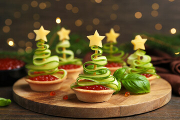 Christmas tree shaped tartlets made with red caviar, cucumber and cheese on wooden table, closeup