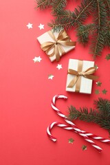 Fir tree branches, gifts and Christmas decor on red background, flat lay