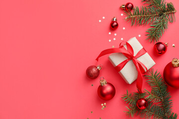 Fir tree branches, gift and Christmas decor on red background, flat lay. Space for text