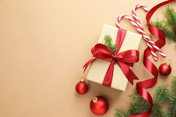 Fir tree branches, gift, candy canes and Christmas decor on beige background, flat lay. Space for text