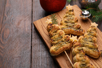 Christmas trees made with puff pastry, pesto sauce, cheese and festive decor on wooden table, closeup. Space for text