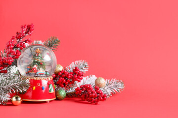 Fir tree branches, snow globe and other Christmas decor on red background. Space for text