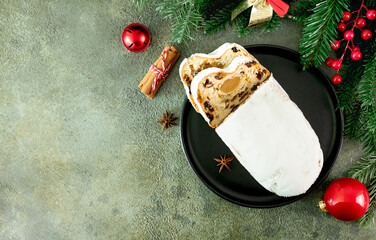 Christmas marzipan stollen decorated with fir branches and holiday ornaments on green background. Top view. Copy space.