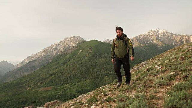 Traveler man walking uphill at sunrise with backpack and trekking poles concept of freedom motivation adventure success morning energy and connection with wild mountain nature