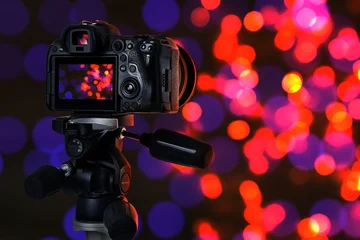 Fotobehang Muziek Professional camera against blurred lights on dark background, bokeh effect  © New Africa