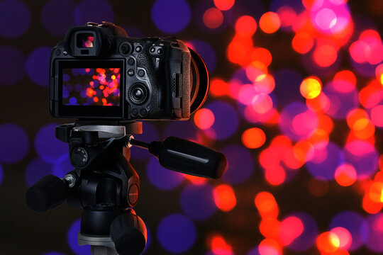 Professional camera against blurred lights on dark background, bokeh effect