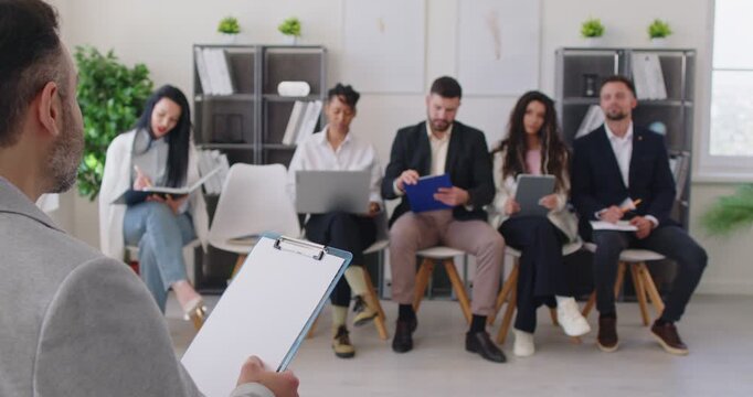 Leader speaking on business training, seminar or presentation to team of corporate employees in office. Group of company staff sitting on chairs with laptop, tablet and paper notes, looking at trainer - Powered by Adobe