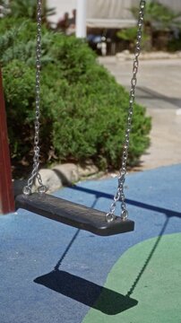 Swing casting shadow on sunny playground with vibrant colors and greenery, emphasizing outdoor leisure in bright weather.