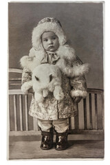 A retro photograph of a child girl wearing a fur-trimmed fur coat, with a fur muff in the form of a toy, 20-30 years of the last century.