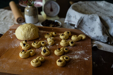 Process of making traditional Swedish saffron buns. S-shaped yeast buns spiced with saffron and decorated with raisins on wooden board.