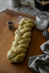 Unbaked challah bread sprinkled with sea salt flakes and cumin on wooden board.