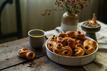 Homemade Swedish saffron buns and coffee on wooden table. Traditional treat eaten on Saint Lucia Day and during Advent. Spiced with saffron and decorated with raisins.