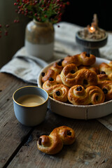 Homemade Swedish saffron buns and coffee on wooden table. Traditional treat eaten on Saint Lucia Day and during Advent. Spiced with saffron and decorated with raisins.