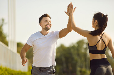Running outdoors, happy sporty couple, fit man and woman happily high fiving, smiling brightly,...