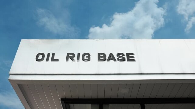 An oil rig base word sign displayed on a large industrial port facility under a clear blue sky, symbolizing logistics, offshore support, energy supply, and maritime operations