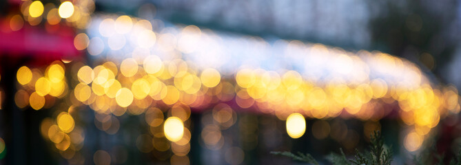 New Year's or Christmas decoration street cafe with light bulbs. Christmas lights on roof of building are out of focus. Narrow banner. Concept of Christmas decorations on street. Bokeh.