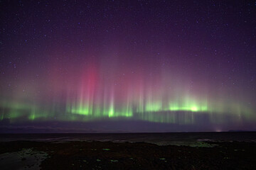 Red and green Northern Lights aurora borealis in the night sky with the sea in the foreground