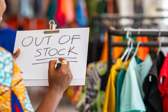 African businesswoman writes "OUT OF STOCK" on a clipboard in her clothing boutique, inventory challenges and supply chain issues in fashion entrepreneurship, SME