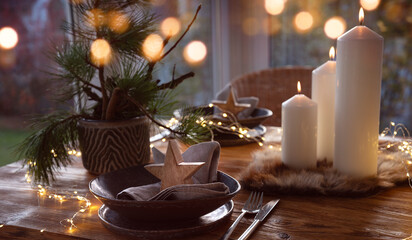 Elegant table decoration for a christmas dinner. Romantic dinner concept with burning candles in the evening at a restaurant. Close-up with golden bokeh lights. Background for seasonal an holiday gast