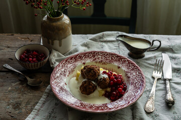 Traditional Swedish meatballs with mashed potatoes, cranberries and creamy gravy in vintage plate on wooden table. Homemade dinner. Comfort food.