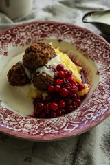 Traditional Swedish meatballs with mashed potatoes, cranberries and creamy gravy in vintage plate on wooden table. Homemade dinner. Comfort food.