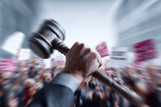 Public riots against the court's decision, people against a criminal law, concept. The judge's hand with a gavel, against a crowd of dissenters, conceptual image