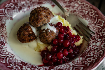Traditional Swedish meatballs with mashed potatoes, cranberries and creamy gravy in vintage plate on wooden table. Homemade dinner. Comfort food.