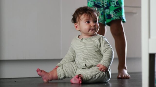 Baby sitting on floor stretching arms for balance, moment of movement and coordination during early developmental stage at home