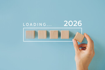 2026 New Year Loading. Female hand moving wooden blocks with Loading bar between 2025 and 2026 on a blue background. Concept for transition, progress, new year, and future plans