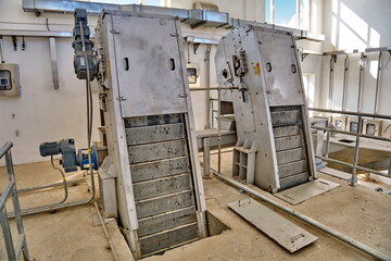WWTP Coarse Mechanical Screening Hall. Two inclined mechanized bar screens with electric drives for removing large debris from wastewater.