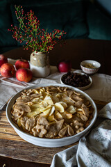 Unbaked homemade apple pie decorated with crust in baking form on rustic kitchen.