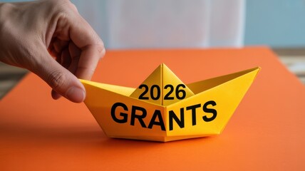 Hand holding yellow paper boat with 2026 grants written on it