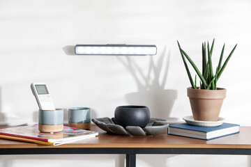 Stylish LED lamp on white wall above wooden table with magazines and decor indoors