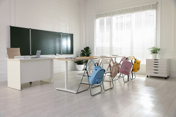 Green chalkboard, backpacks and stylish furniture in classroom. Mockup for design