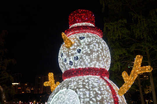 A bright LED snowman with a red hat and scarf glows at night. Holiday decoration brings cheerful winter spirit to the city. - Powered by Adobe