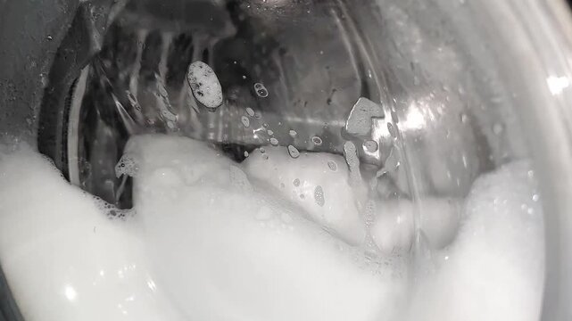 white soapy detergent foam spinning inside washing machine, slow motion closeup view